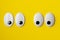 Two pairs of funny googly or wiggle eyes looking towards each other on yellow background, minimal concept