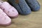 Two pairs of home slippers, pink womens and gray mens on a brown wooden floor. Cozy, warm and comfortable domestic shoes