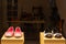 Two pairs of shoes are lying on display pedestals in a window display of a shoemaker workshop at night.