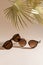 Two pairs of women sunglasses on beige background with golden palm leaves. Minimalism, summer fashion concept. Trendy sunglasses