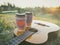 Two paper coffee cup in knitted cozy sleeves standing on guitar. Outdoor picnic sunset scene