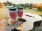 Two paper coffee cup in knitted cozy sleeves standing on guitar. Outdoor picnic sunset scene