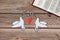 Two paper doves carry branches, an open Holy Bible Book, and a red heart on a wooden background