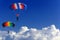 Two parachutists soar on colorful parachutes across the boundless blue sky against the background of white fluffy clouds