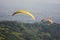 two paragliders on yellow and red parachutes on the background of green mountains and a city in the valley