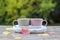 Two pastel cups with hot tea in white knitted scarf on wet table with pink and yellow leaves after rain