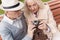 Two pensioners are sitting on the bench and studying a vintage camera. They are going to take a few photos