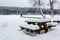 Two people looking at the landscape. Wood bench and table covered of snow in front of a frozen lake