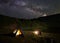 Two people at night camping in mountains near the lake under sky strewn with stars and bright milky way