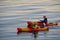 Two people paddle their colourful kayaks in the ocean at sunset