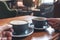 Two people`s hands holding coffee and hot chocolate cups on wooden table in cafe