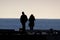 Two people in silhouette talking on seaside pier.