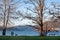 Two people walk their dog along waterfront with snow capped mountains in background