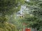 A two person lift cab is lifted on a cable against a background of green coniferous trees on a Sunny summer day