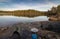 Two persons sitting at the edge of lake making coffe on a camp stove, pine forest in the wilderness of Norway