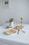 Two pieces of cake on white plates golden forks a vase with a flower and coffee and a golden candlestick on a white table