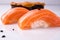 Two pieces of Japanese salmon nigiri sushi, piece of uni gunkan on a white reflective surface decorated black tobiko. Close up.