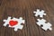 Two pieces of puzzle forming red heart on rustic brown wooden surface, heart on pieces of jigsaw, romantic background for