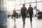 Two pilots walking along the airport terminal following the stewardess