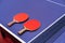 Two pingpong table tennis rackets for playing are laid on next to net on the blue table. This is one of ping pong sports equipment