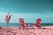 two pink chairs sit on the beach in front of a palm tree