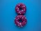 Two pink donuts decorated with glaze hearts laid out as the number eight isolated on a blue background top view