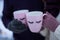 Two pink mugs with eyelashes in the hands of people
