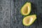 Two pitted avocado halves on a black wooden table. The view from the top