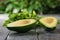 Two pitted avocado halves and parsley on a black wooden table. The view from the top