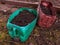 Two plastic cans cut in half and reused and repurposed as flower pots or planters filled with soil in the garden