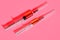 Two plastic disposable syringes with red medicine on a pink back