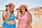 Two plus size overweight sisters twins women listening to a voice message on the phone at the beach on summer holidays