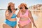 Two plus size overweight sisters twins women sending a voice message on smartphone the beach on summer holidays