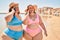 Two plus size overweight sisters twins women speaking on the phone at the beach on summer holidays