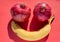 Two pomegranates and a banana on red in smiling form