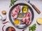 Two pork steaks with oil and spices in a pan with lemon, salt and meat fork wooden rustic background top view close up