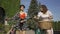 Two positive women in bright dressing talking while leading their bicycles on the narrow road on the street. Rural life