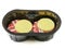 Two premium beef burgers wrapped in rashers or bacon and butter and cheese on top in a black plastic tray on white background.