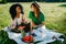 Two pretty charming multi-race girlfriends with natural make-up and beautiful smile having fun on the picnic while