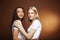 two pretty diverse girls happy posing together: blond and brunette, caucasian and asian on brown background, lifestyle
