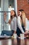 Two pretty female students sitting together on desk in classroom, a girl pointing at light bulb like having a brilliant