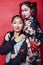 Two pretty geisha girls friends: modern asian woman and traditional wearing kimono posing cheerful on red background