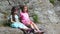 Two pretty girls, kids, sit on a ledge in the rock., a beautiful orange mountain butterfly whirls and flies over a child