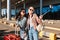 Two pretty girls in sunglasses joyfully taking photo on cellphone together with suitcase and backpack on shoulder near