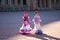 Two pretty little girls dancing flamenco dressed in typical gypsy costumes walk hand in hand through a famous square in Seville.