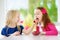 Two pretty little girls eating raspberries at home. Cute children enjoying their healthy fresh organic fruits and berries.