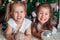 Two pretty sisters laugh and show teeth next to Christmas tree