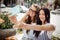 Two pretty thin girls with long dark hair,dressed in casual stye,sit at the bench and take a selfie,