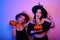 Two pretty witch poses with pumpkins for a Halloween photo. Girls in witch hats in neon dance at the party