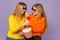 Two pretty young blonde twins sisters girls in 3d imax glasses watching movie film, holding popcorn  on pastel
